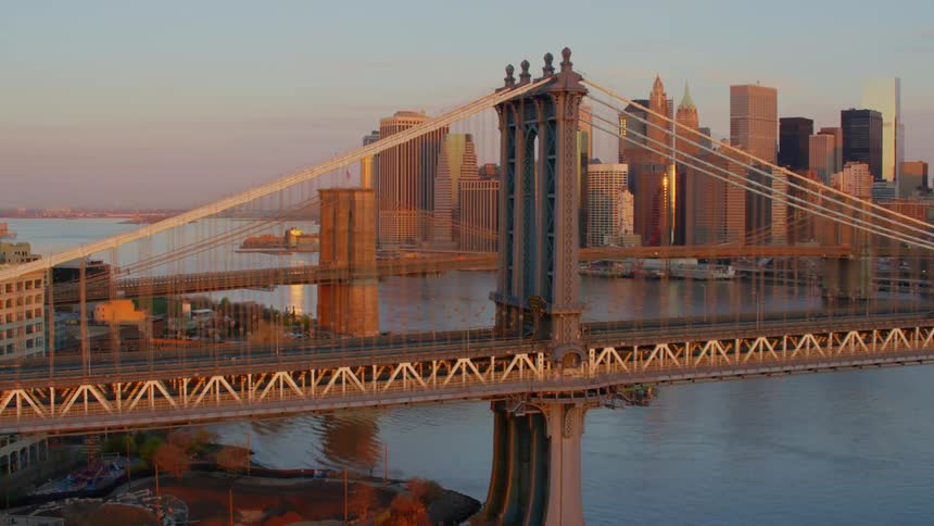 Manhattan bridge and brooklyn bridge in front of the new york city skyline at sunset