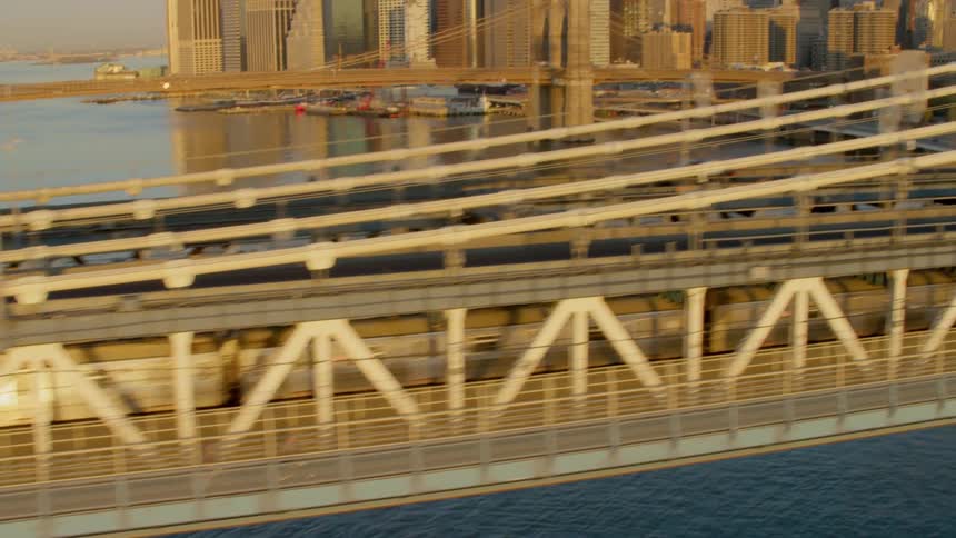 A suspension bridge over water leads to a large downtown city
