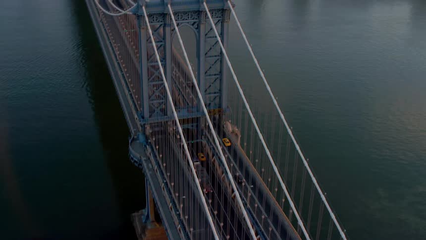 Traffic drives across a suspension bridge over a river and into the city