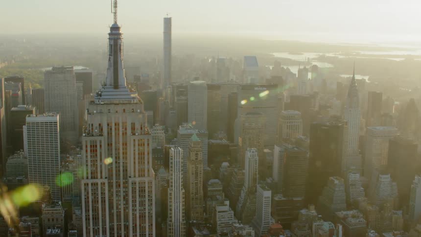 A tall skyscraper with a steeple stands above other buildings in a city near a river