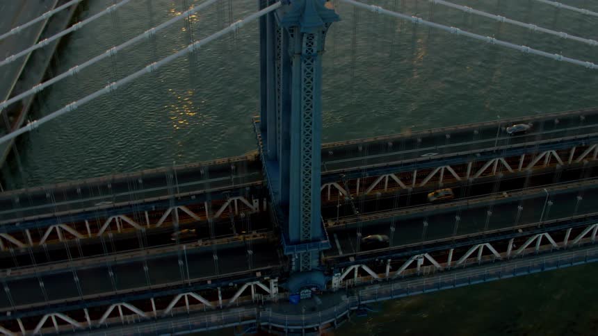 Traffic moves across a suspension bridge over a river that goes into a city