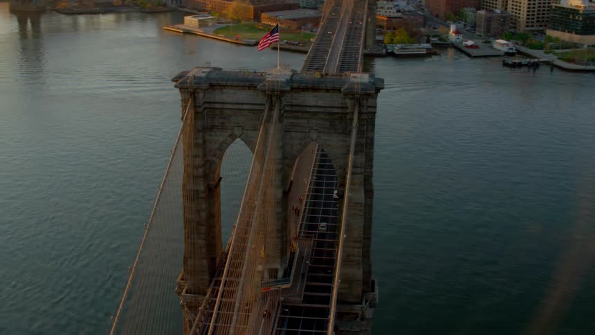 A suspension bridge filled with traffic stretches across a river next to a city