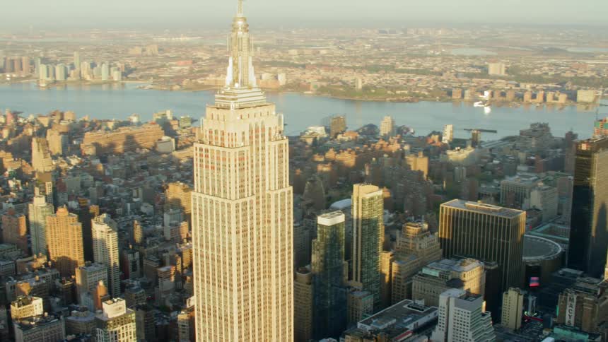 Empire state building sits in center of downtown near river on foggy day