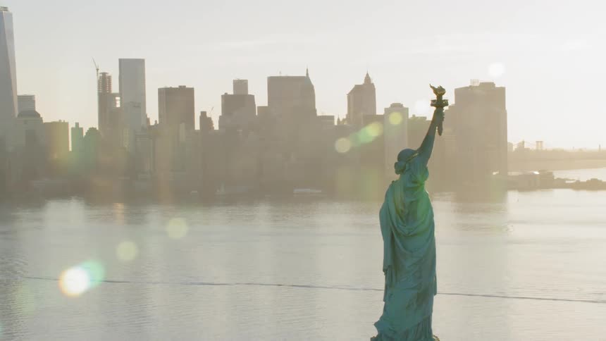 The statue of liberty with the city skyline behind on a glaring sunny day