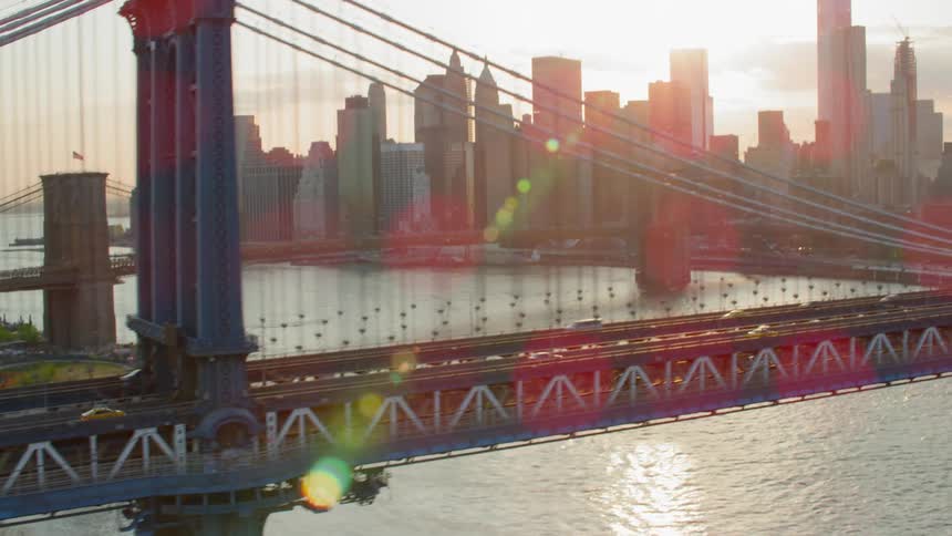 Cars travel on a bridge across the river towards the city as the sun shines down and reflects off the water