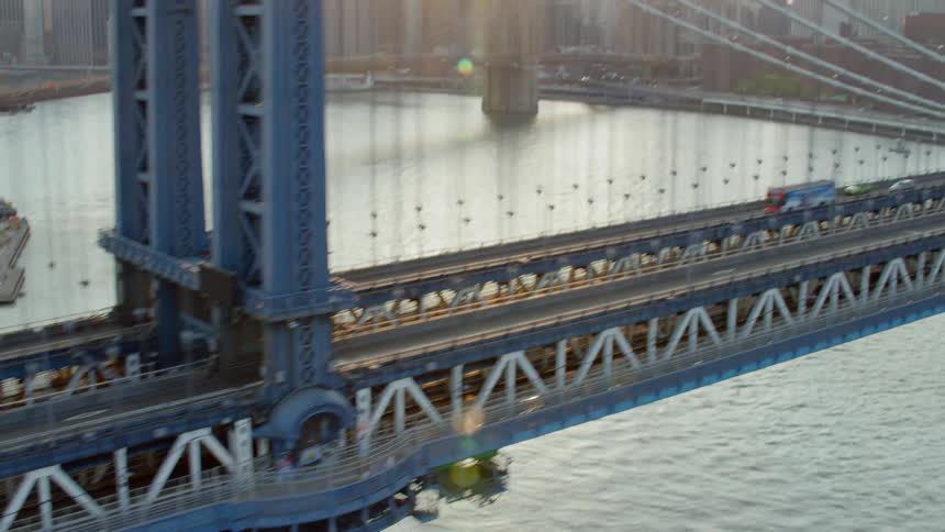 Suspension bridge filled with traffic stretches across a river by a city