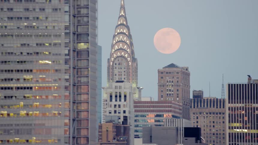 The moon is visible over a downtown city filled with tall skyscrapers