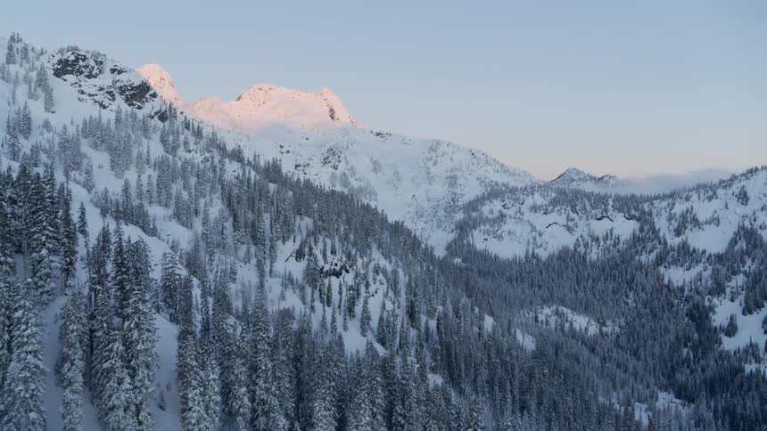 Snow blankets the forested slopes of a deep mountain valley