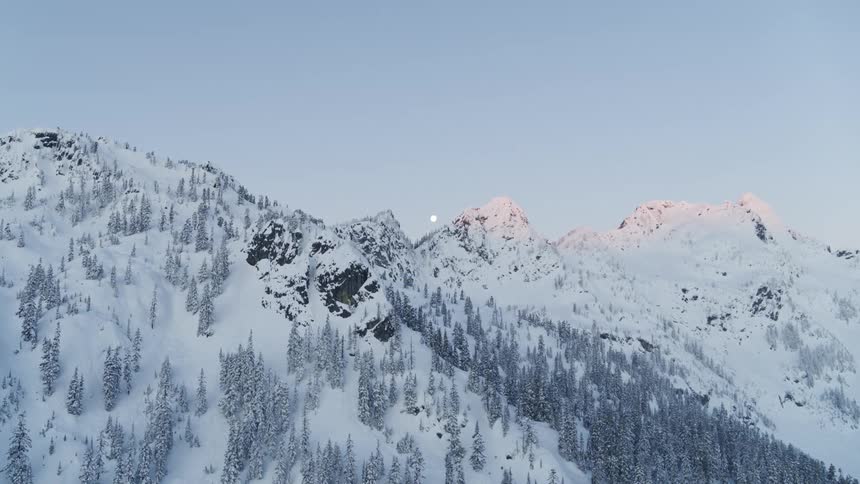 A full moon glides between mountaintop peaks at first light on a crisp winter morning