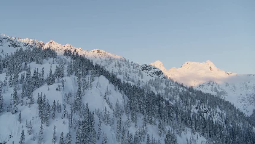 Pullback reveal of a winter mountain valley at sunrise as the moon floats behind distant peaks