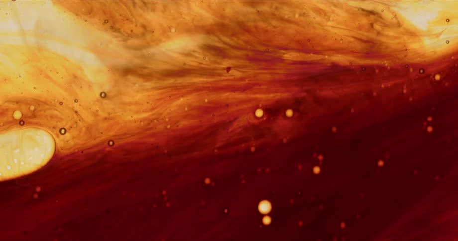 Red orange and yellow liquids swirl together to form a pattern dotted with bubbles