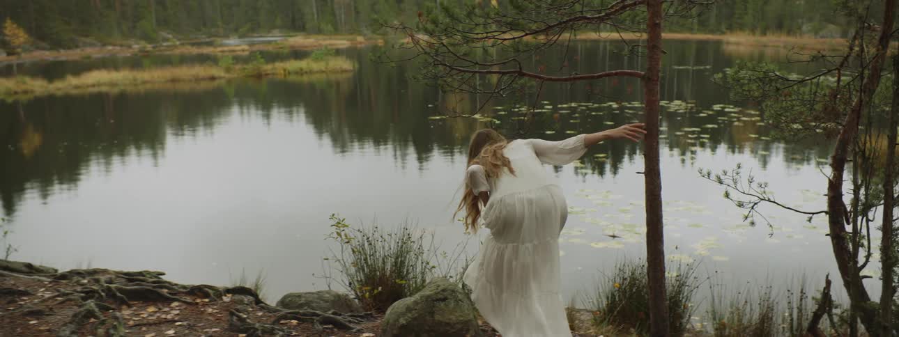 A woman with a white dress walking towards a lake