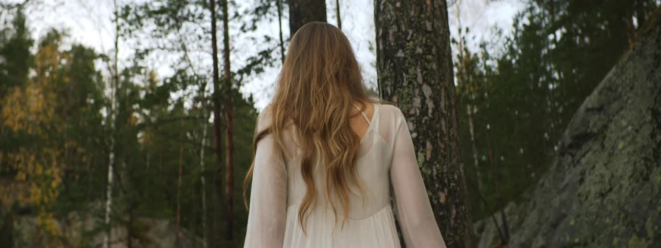 A woman in a white dress walks alone in a forest