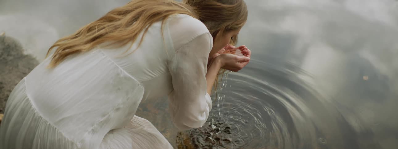 Woman scooping up water from lake and drinking from palm of her hands