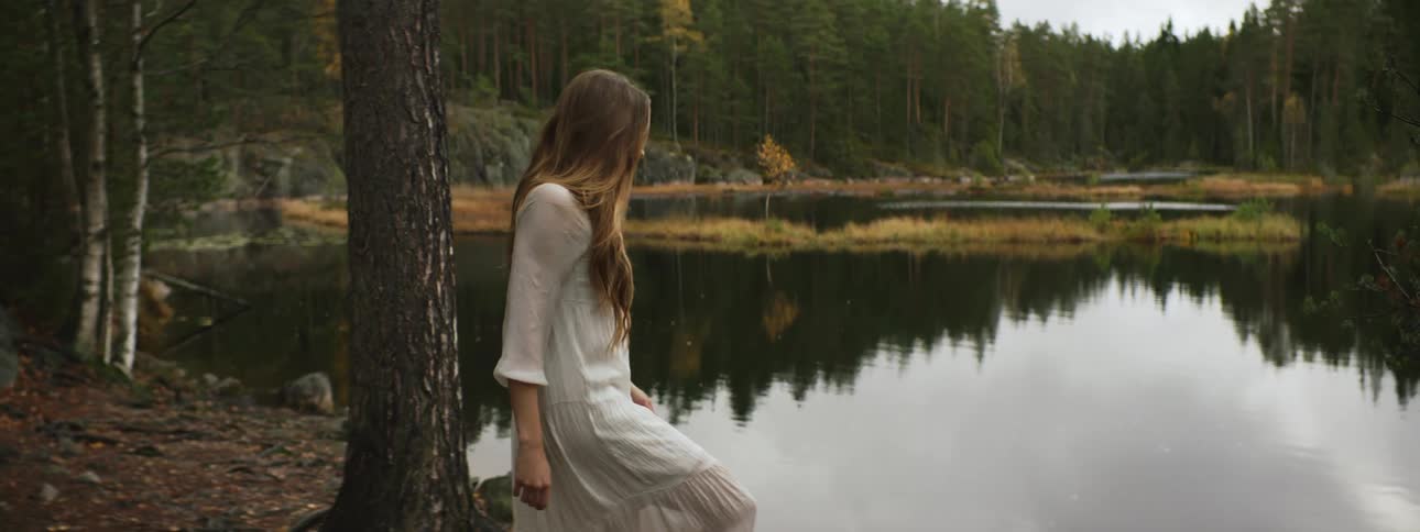 Woman in dress slowly walks near lake on a pine forest