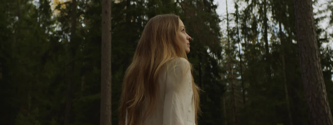 Blonde woman inwhite dress standing in forest looking around