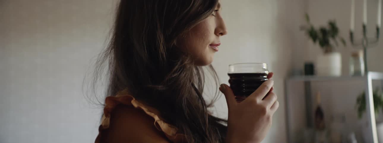 A brunette woman with long hair stands in a room holding a drink