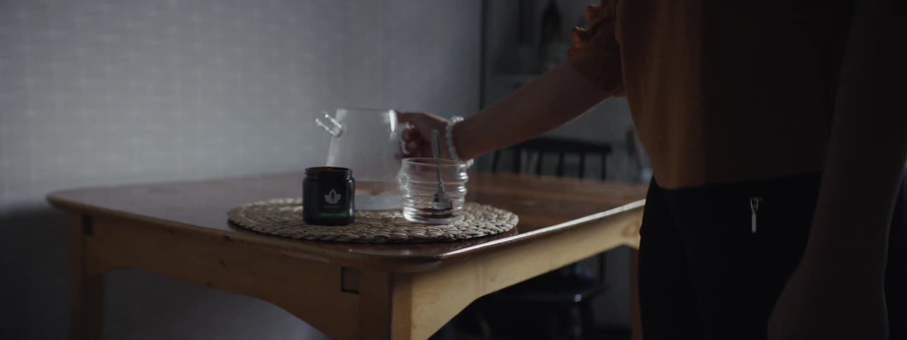 A woman spoons instant coffee crystals into a cup and pours hot water from a clear glass carafe