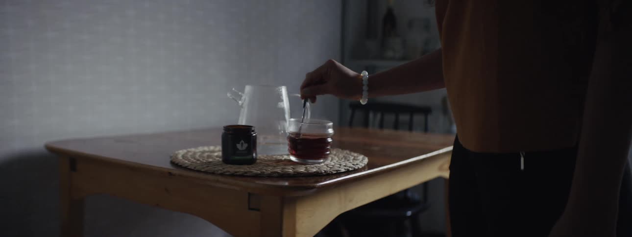 A woman pours a cup of tea into a mug and gives it a stir