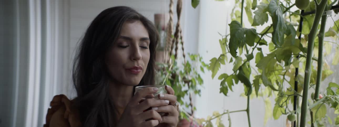 A brunette woman drinks on a balcony