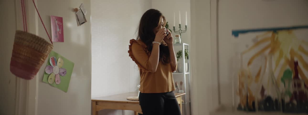 A woman in a room standing drinking tea
