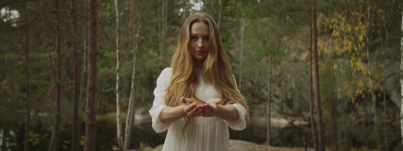 A woman standing in the woods with a white dress holding something in her hands