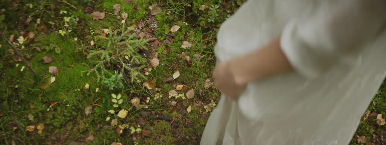 A white woman in a dress walks over grass and leaves