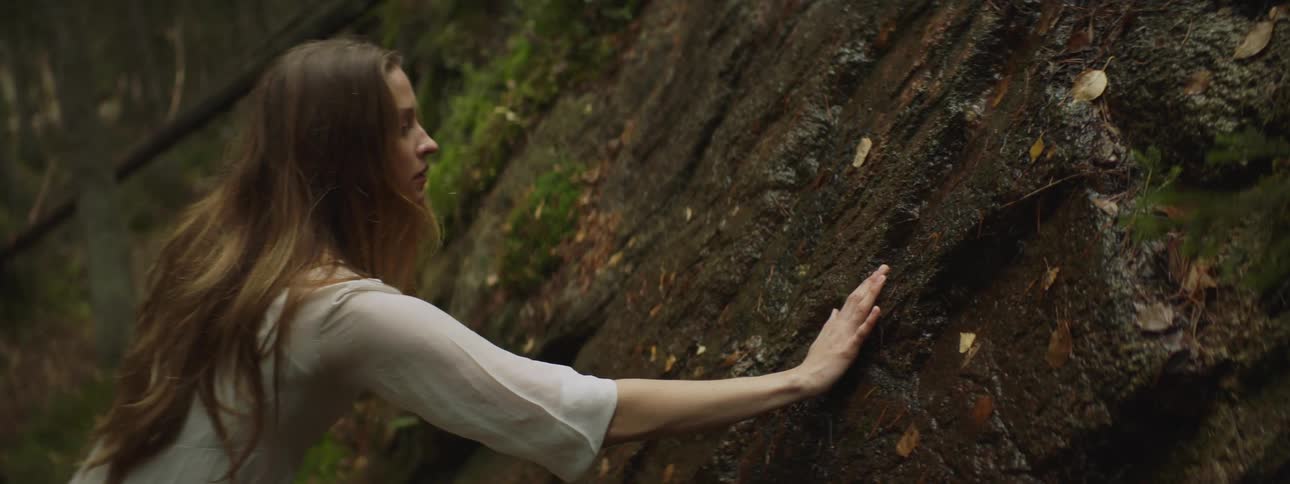 Woman wearing a dress touches a small stream of water running on a rock in the forest
