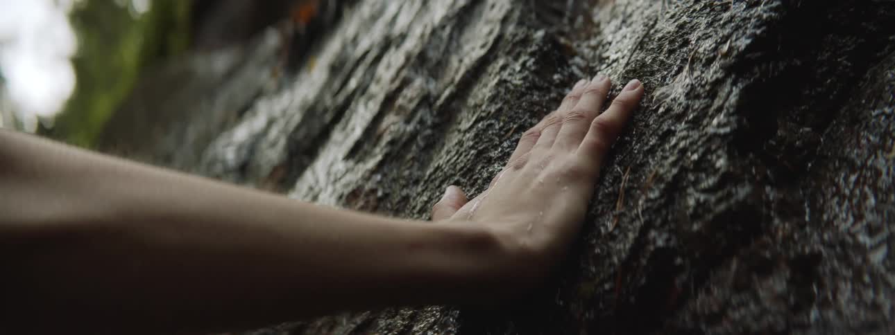 Person touches very small stream of water flowing down sloping rock
