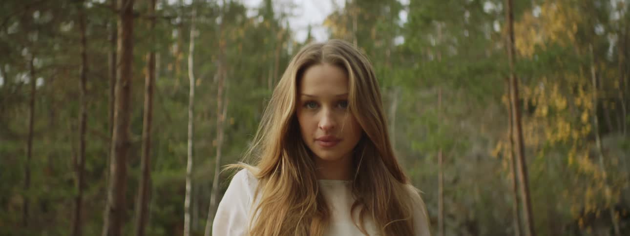 Woman with long hair wearing white dress stand still in the forest at day