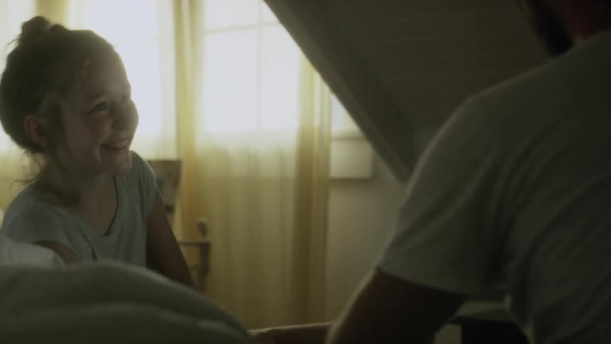 A girl sits on a bed next to a man and laughs