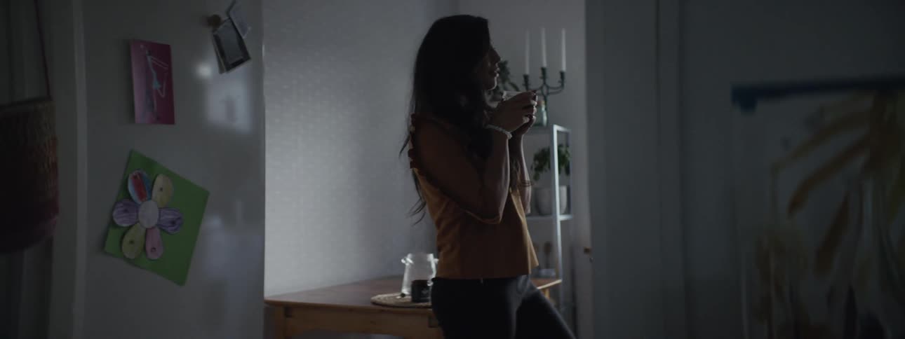 A woman picks up a coffee mug from a table and starts to drink