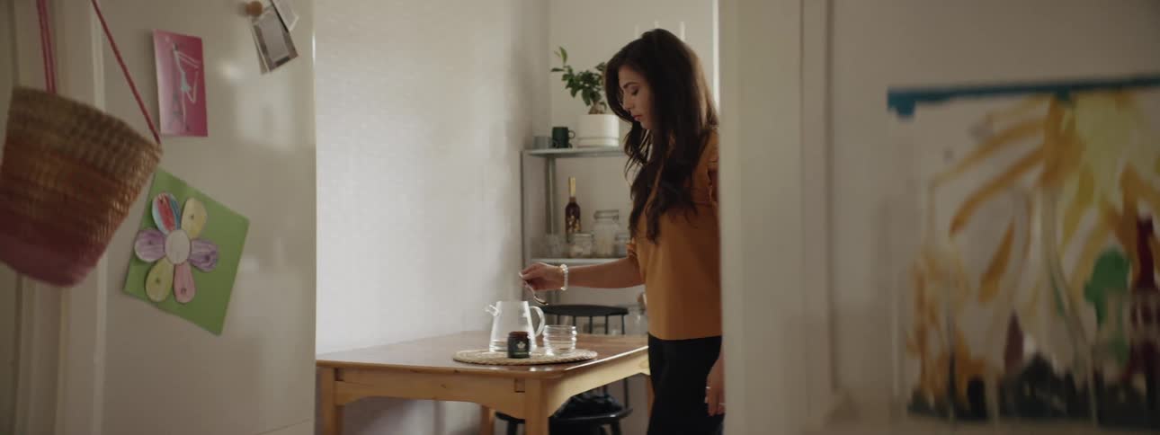 A woman stands at a table spooning sugar into a clear glass tea cup on a tray