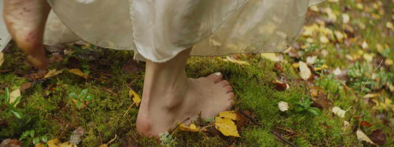 A woman walks barefoot through a lawn covered with leaves