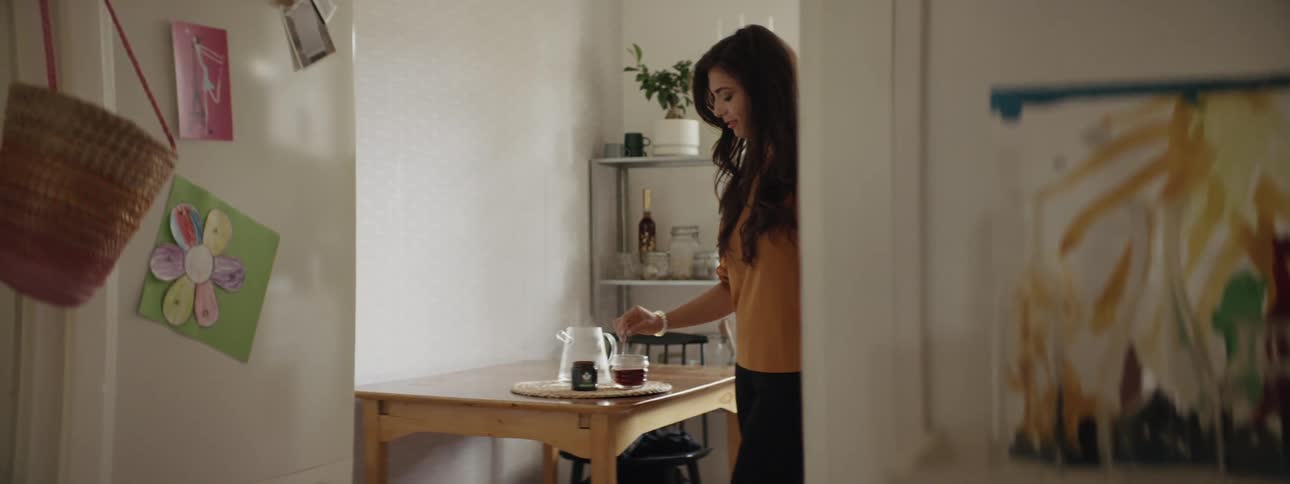 Woman stands next to table stirring beverage in glass cup