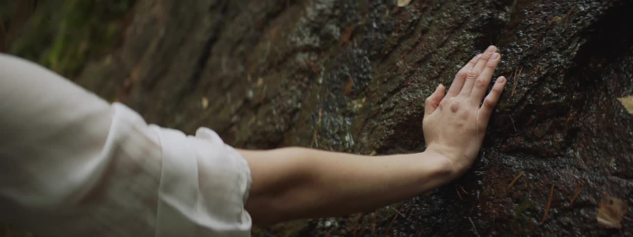 A woman rests her hand on a rock with water running down it