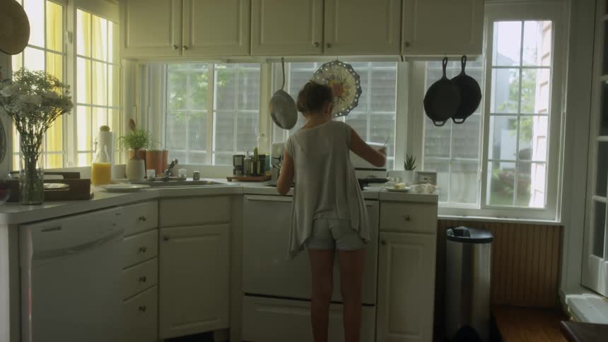 A woman cooking in a kitchen with many windows