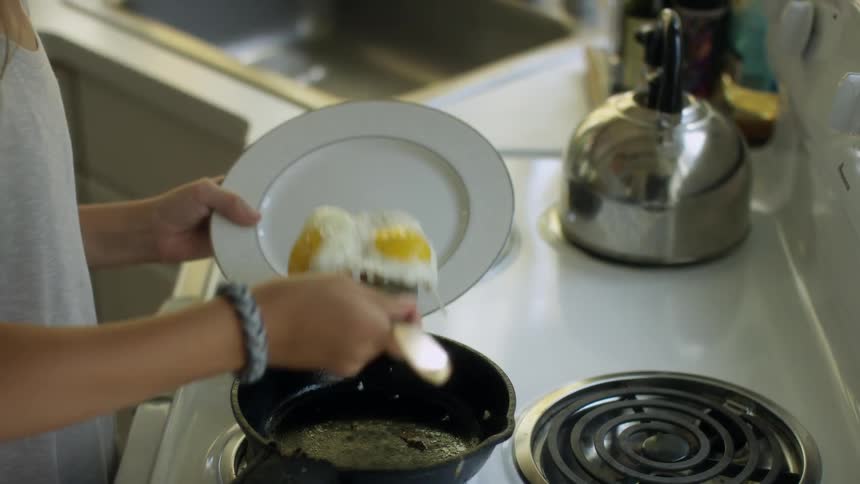 A woman puts eggs from a pan onto a plate