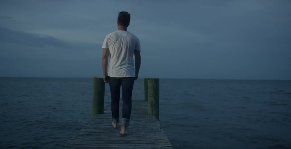 A man is walking across a boardwalk towards the water