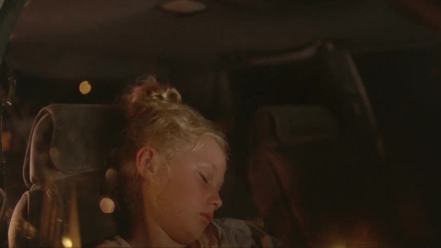 A girl is sleeping in a car as a man gets in and sits