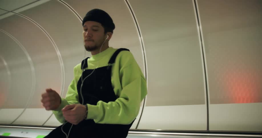 A man is sitting on the railing of a moving sidewalk listening to music