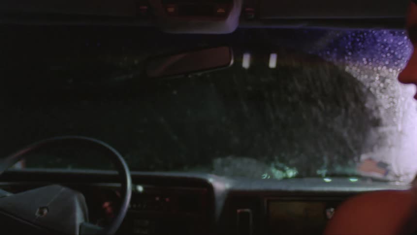 A man is standing outside of a vehicle in the rain as a woman watches inside