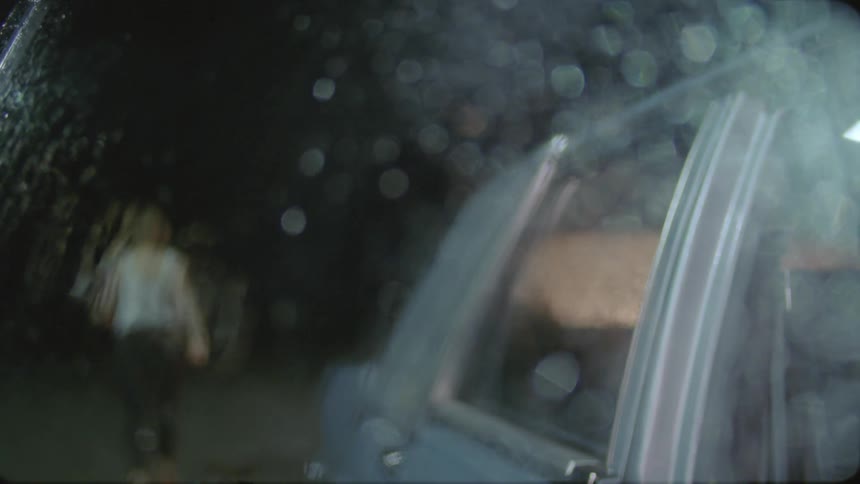 A woman sitting in a car looks around then gets out of the car and walks off in the rain