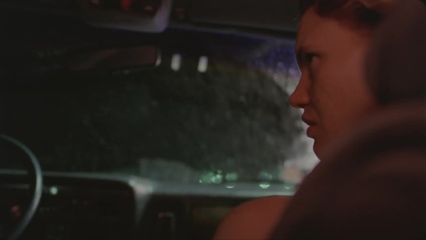 A woman sits inside a car distraught as it rains outside