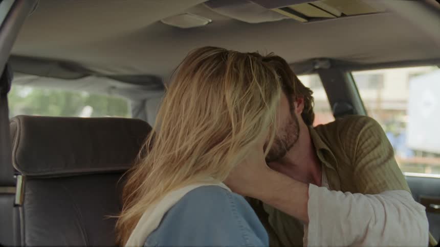 A man and woman kiss in a car in the day time