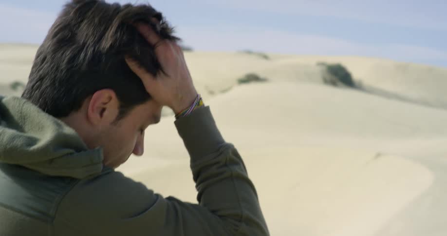 A man sits in the desert with his hand on his head