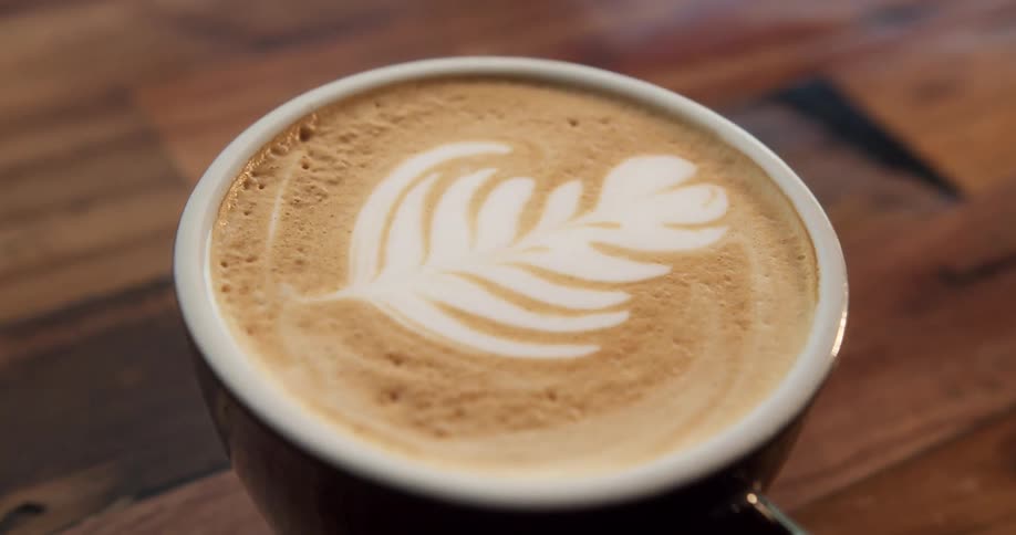 A leaf design is seen in the foam of a cup of coffee