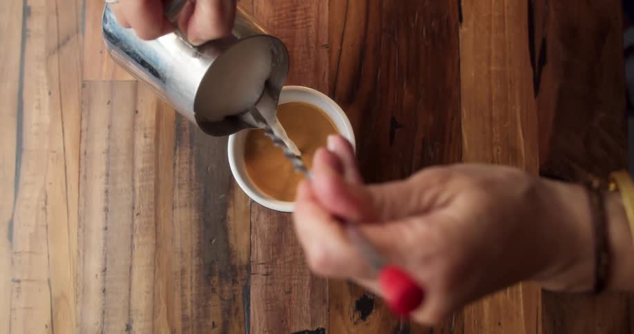 Creamer is poured into a cup of coffee on a wood table