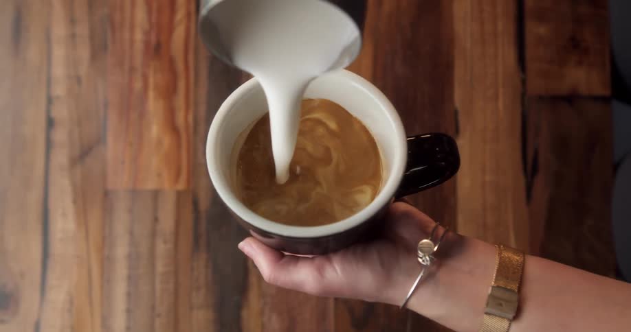 A person adding cream to a cup of coffee