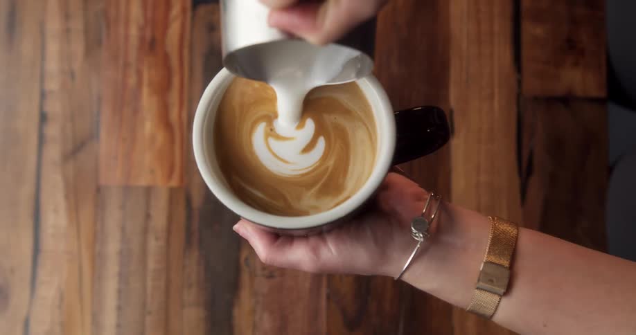 A woman decorates a latte with foam art